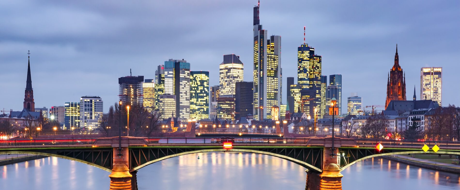 Picturesque view of Frankfurt am Main skyline and Ignatz Bubis Brucke bridge during evening blue hour with mirror reflections in the river, Germany